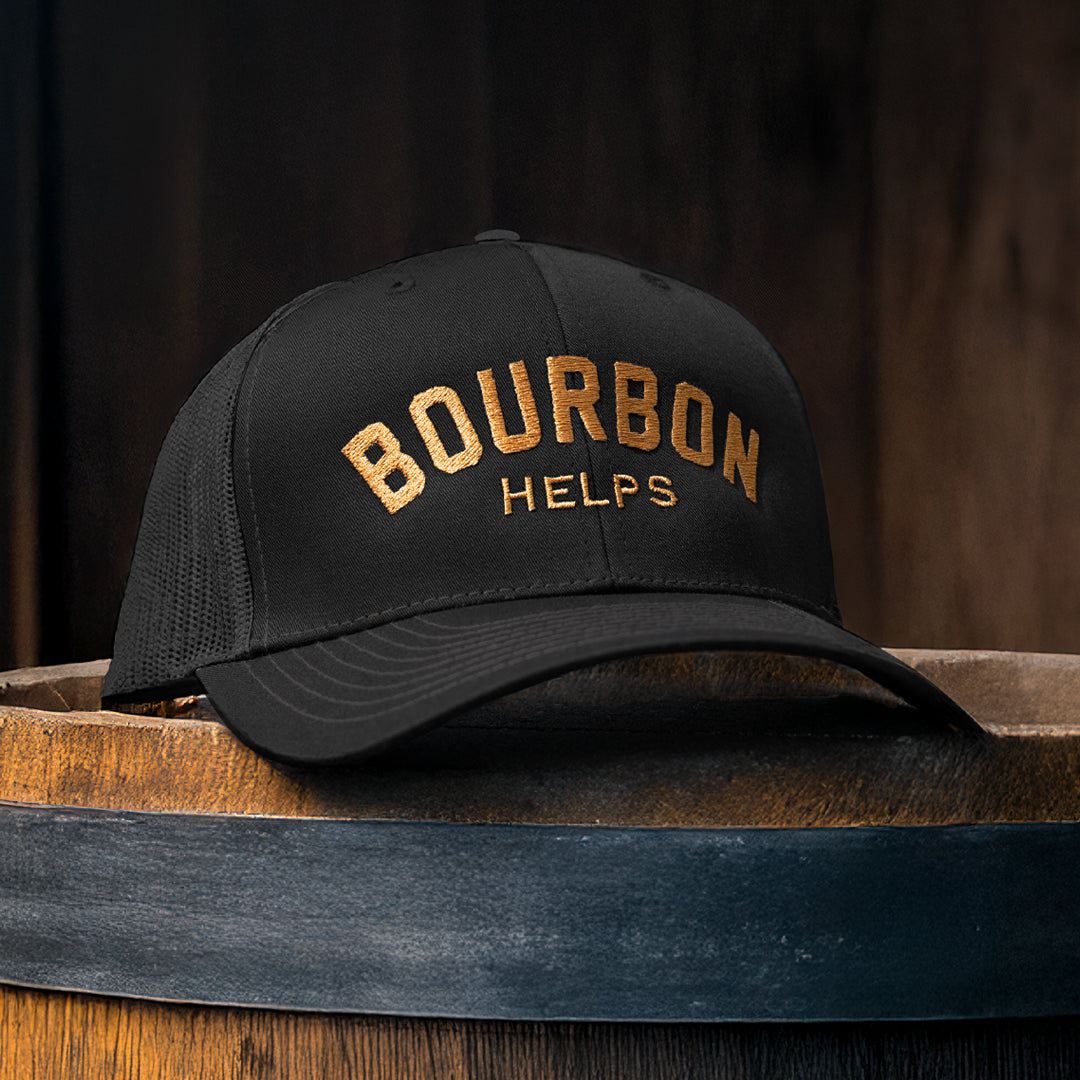 Black cap with 'Bourbon Helps' text on a wooden barrel against a dark background