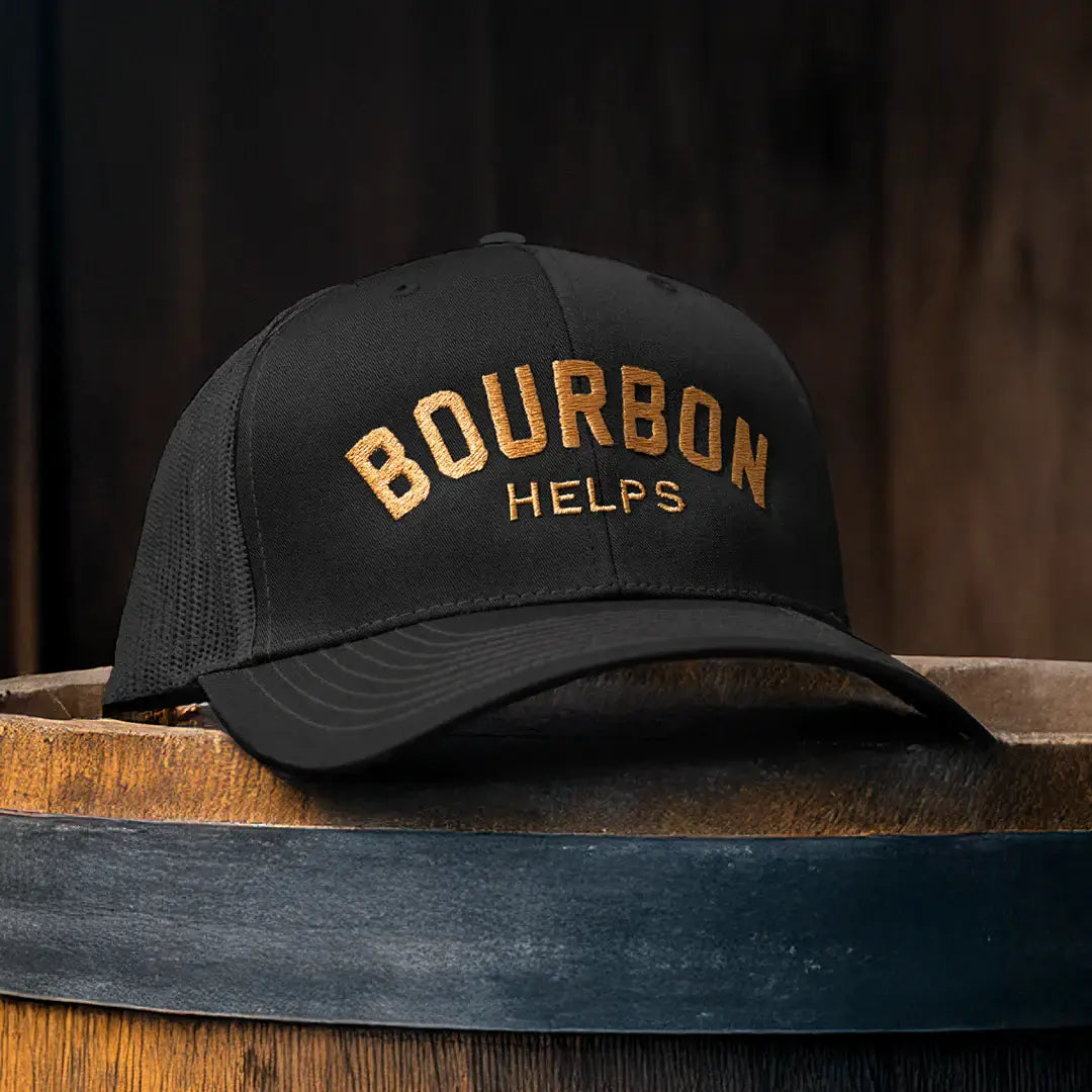 Black cap with 'Bourbon Helps' text on a wooden barrel against a dark background