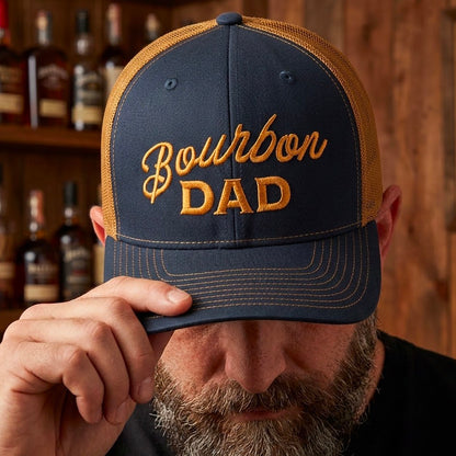 A person wearing a Bourbon Dad Trucker Hat in navy and caramel, with bold embroidery, showcasing a casual style.