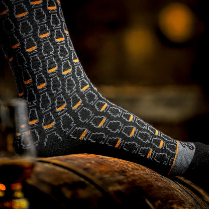 Black bourbon sock with a whiskey glass pattern on a wooden barrel surface with a blurred background