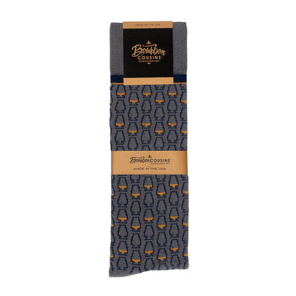 Gray socks with a navy blue pattern of whiskey glasses packaged with bourbon cousins branding
