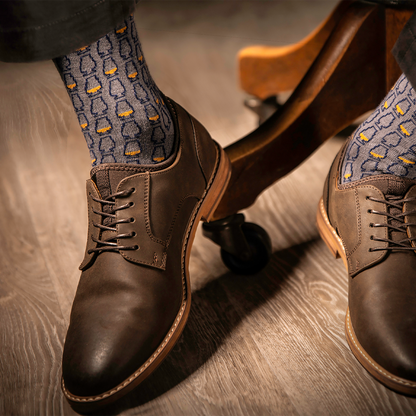a model wearing brown colored shoes highlighting gray socks with a whiskey glass pattern on a wooden floor