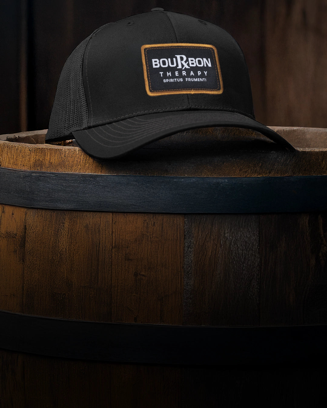 Black bourbon cap with 'Bourbon Therapy' patch on a wooden barrel