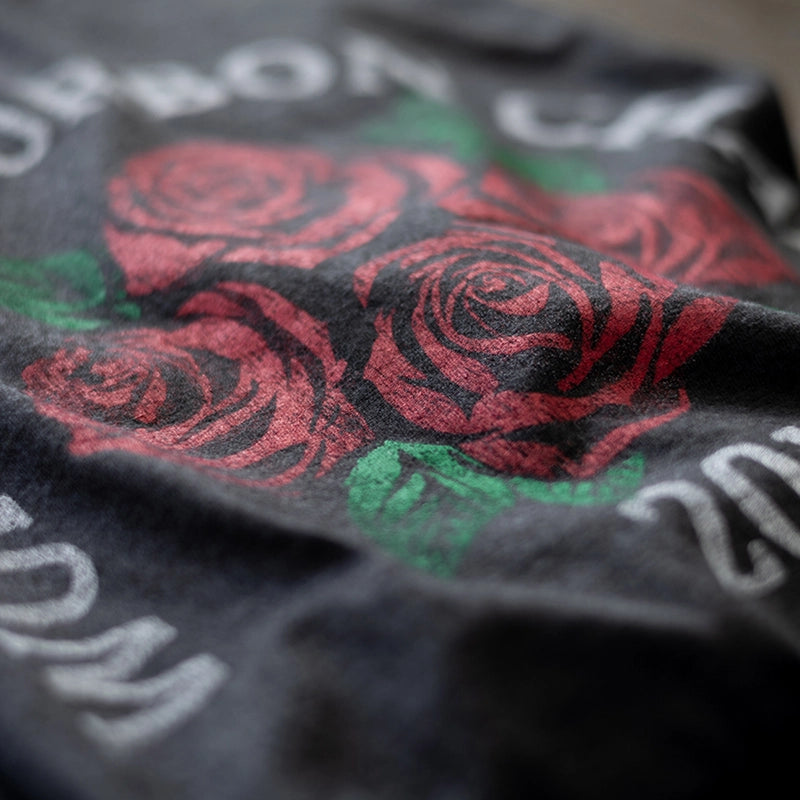 Close-up of a black fabric with four roses bourbon shirt and partially visible text.