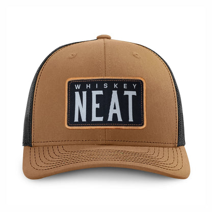 A caramel and black richardson 112 trucker hat with a rectangular front patch reading 'WHISKEY NEAT' in white text on a black background, shown on a clean white background.