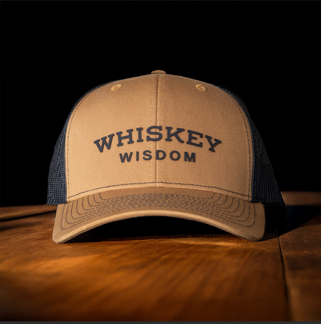 Whiskey Wisdom bourbon hat sitting on a rustic wooden bar top next to a glass of whiskey.