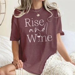 Person wearing a maroon t-shirt with 'Rise and Wine' text, sitting on a white surface.